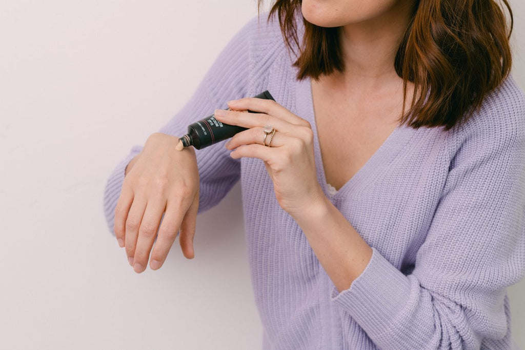 Woman with brunette hair applying Shine Cosmetics Bb Cream to her hand to see if it is a correct color match.