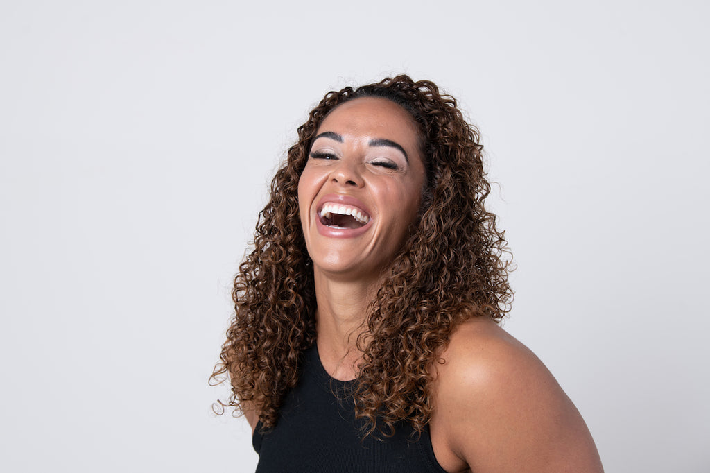 Woman and mother with naturally curly brown hair smiling and laughing.